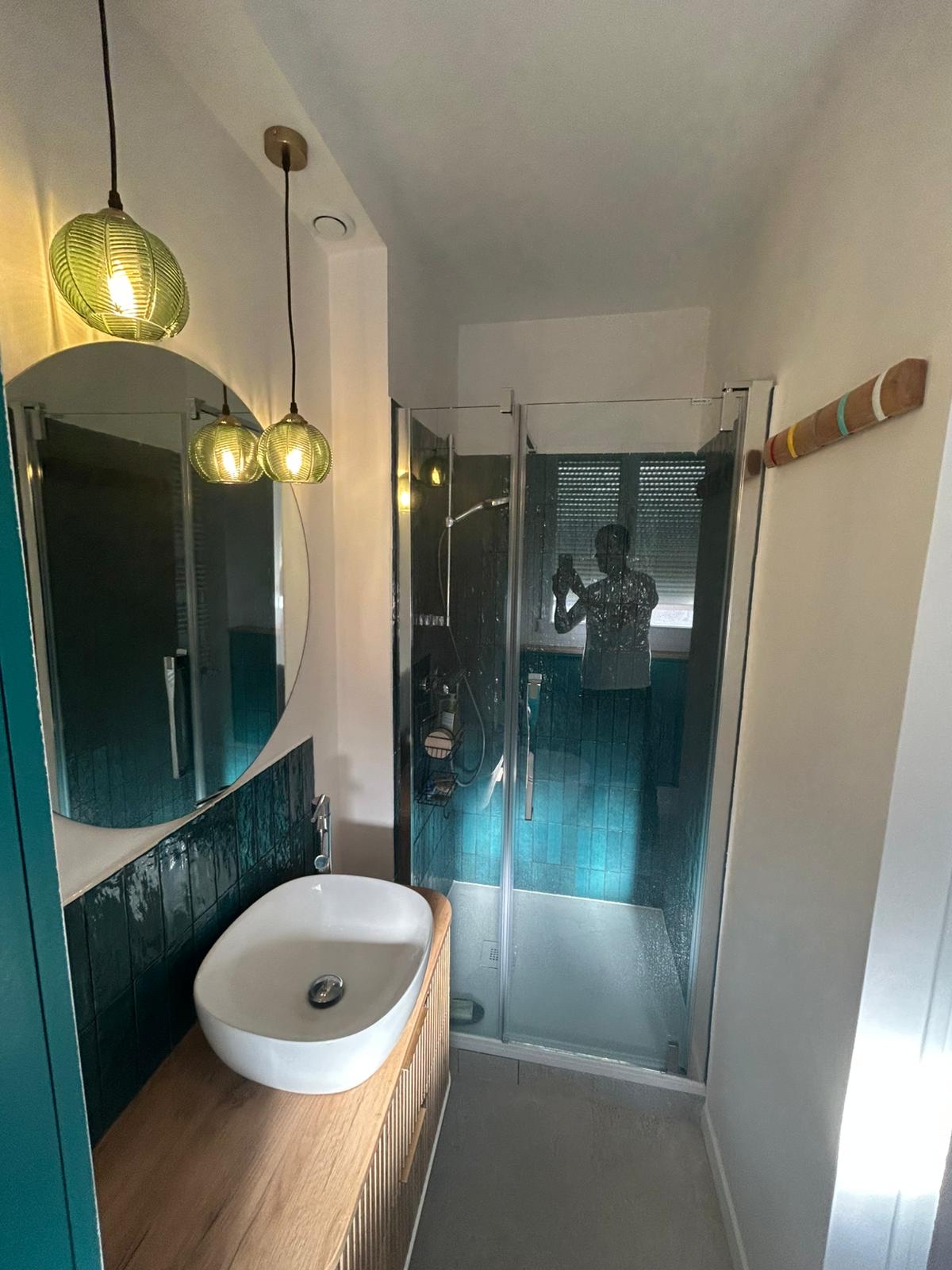 Salle de bain après rénovation avec douche vitrée et faïence vert profond