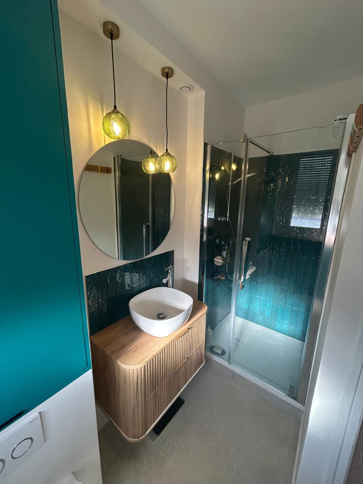 Salle de bain après rénovation avec meuble vasque bois, miroir rond et suspensions