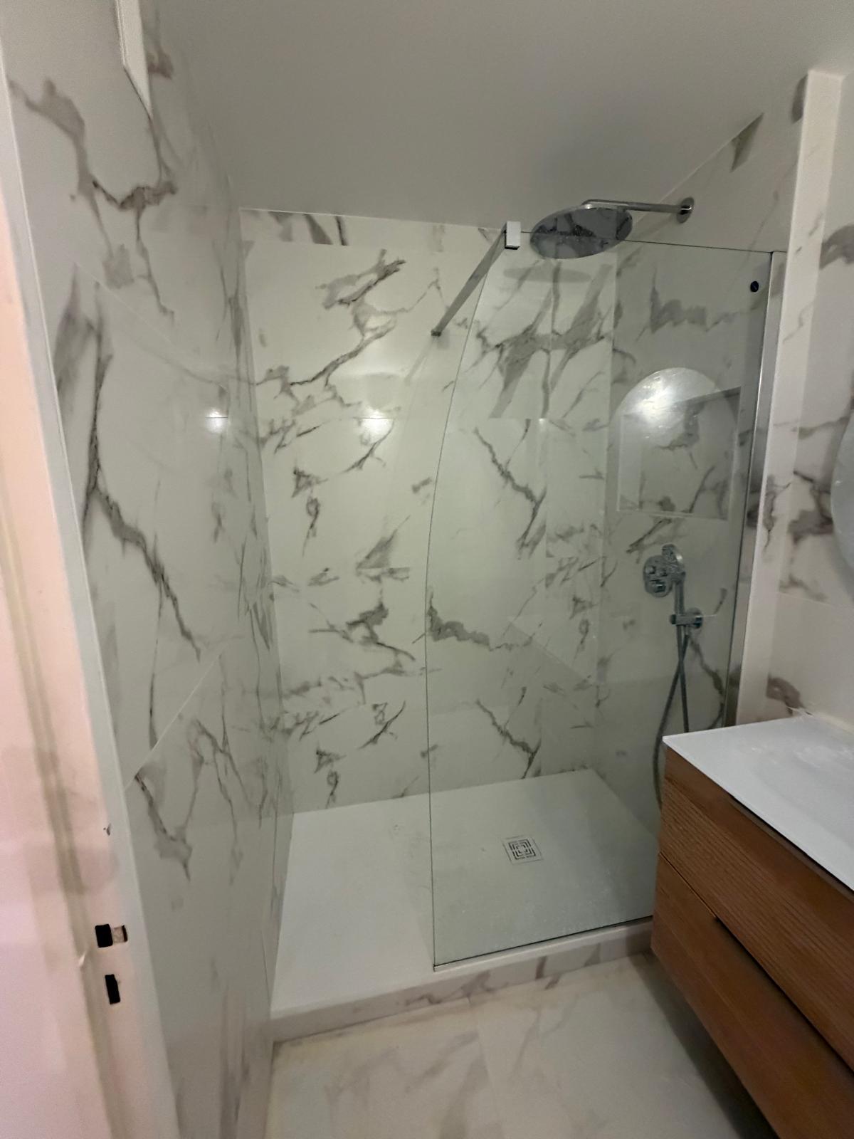 Salle de bain rénovée avec carrelage effet marbre, douche vitrée et meuble vasque bois